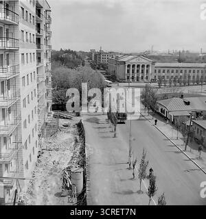 Ein Hochwinkel-Schwarzweiß-Archivfoto aus den 1980er Jahren, das einen Panoramablick auf Sloviansk in der ukrainischen SSR bietet. Der Mittelpunkt ist das monumentale Gebäude des Landwirtschaftskollegs, ein Paradebeispiel der neoklassischen Architektur des Stalinismus mit seinem großen Säulengang. Das Bild fängt die umliegende Stadtlandschaft der Svobody Street ein und zeigt einen Kontrast zwischen dem Grand College, funktionalen Wohnblöcken aus der Sowjetzeit und einer nahe gelegenen Baustelle. Die industrielle Skyline im Hintergrund stellt die Stadt fest in den Donbass und zeigt ihre einzigartige Mischung aus educ Stockfoto