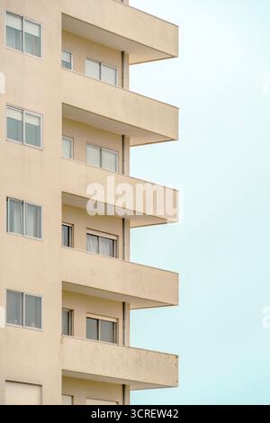 Minimalistische Fassade eines typischen modernen Apartmentgebäudes mit sich wiederholenden Balkonen und Fenstern vor einem klaren hellblauen Himmel Stockfoto