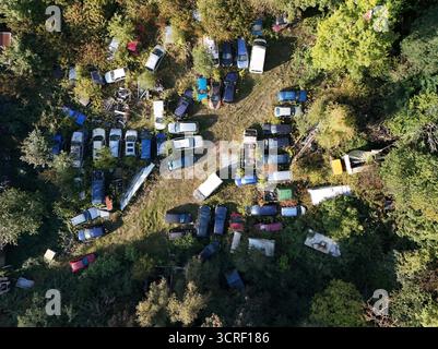 Aus der Vogelperspektive des verlassenen Auto-Schrottplatzes, der vom Wald bedeckt ist Stockfoto