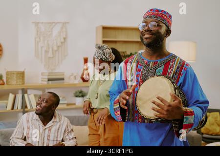 Junger Schwarzer, Der Drum Spielt, Während Freunde Kwanzaa Drinnen Feiern Stockfoto
