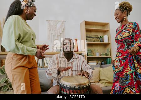 Junger Schwarzer Mann, Der Drum Spielt, Während Zwei Junge Schwarze Frauen Kwanzaa Feiern Stockfoto