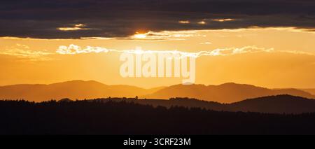 Sonnenuntergang über sanften Hügeln mit einem dramatischen Himmel. Warmes Licht wirft lange Schatten und schafft eine ruhige und malerische Landschaft. Stockfoto