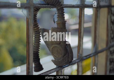 Zerstörte antike Gasmaske mit gewelltem Schlauch, hängt vom Fabrikfenster mit kaputten Glasfliesen. Postapokalyptischer Bokeh-Hintergrund. Stockfoto