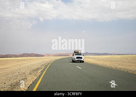 Im Inneren von Sossusvlei ziehen sich Schotterstraßen und ein Auto durch rote Dünen nach Deadvlei, Big Daddy und Sesriem Canyon, wo Sie malerische, staubige Wüstenausblicke genießen können. Nami Stockfoto