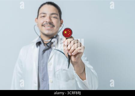 Lächelnder Arzt zeigt Stethoskop mit China-Flagge. China nationale Gesundheitsversorgung Stockfoto