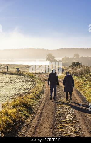 Zwei Leute laufen auf Schotterwegen auf dem Land an einem nebeligen Herbstmorgen, Schweden Stockfoto