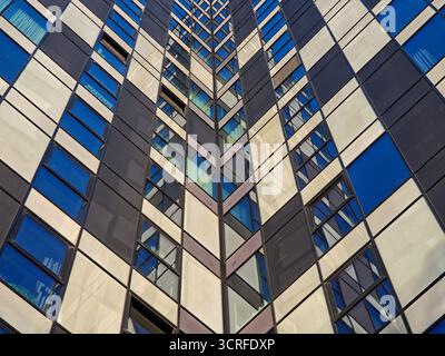 Abstrakte Ansicht einer modernen Wolkenkratzerfassade mit einem sich wiederholenden Schachbrettmuster aus dunklen Paneelen und reflektierenden Fenstern in Blau- und Weißtönen Stockfoto