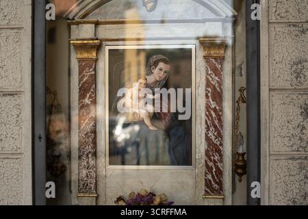 Madonna- und Kindergemälde sind in einem kleinen traditionellen Schrein mit Marmor und vergoldeten Details zu sehen, die das Licht der städtischen Umgebung reflektieren Stockfoto