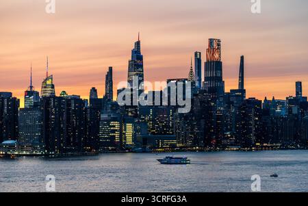Blick auf die Skyline der Stadt mit funkelnden Lichtern, die sich unter einem lebendigen Sonnenuntergang auf dem Wasser spiegeln, das die Gebäude in New York, New York, USA beleuchtet. Stockfoto
