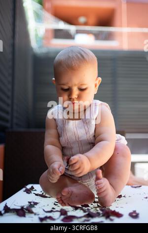 Mädchen, das draußen auf einem Tisch sitzt und mit roten Blumenblättern spielt Stockfoto