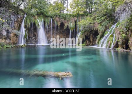 Blick auf die kaskadierenden Wasserfälle, die in einen kristallklaren türkisfarbenen See tauchen, im Kontrast zu dem umliegenden üppigen Grün, Plitvicer Seen, Lika-Senj, Kroatien. Stockfoto