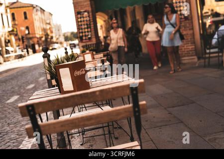 padua, italien 1. oktober 2025: kaffeetische und -Stühle auf der Kopfsteinpflasterstraße padua, sonnendurchflutete Sitzplätze im Freien mit unscharfen Fußgängern und historischem italienisch Stockfoto
