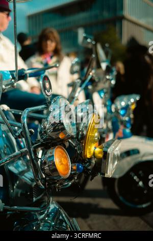 London, Großbritannien – 2025.09.27 – Nahaufnahme mehrerer verchromter Scheinwerfer und Lampen eines Oldtimer-Rollers, die die Menge beim Oldtimer-Boot-Sale widerspiegeln. Stockfoto