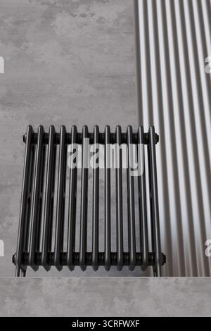 Schwarzer Heizkörper steht vor einem minimalistischen grauen Hintergrund und zeigt sein modernes Design. Diese stilvolle Heizlösung verschönert jeden Innenraum mit Stockfoto