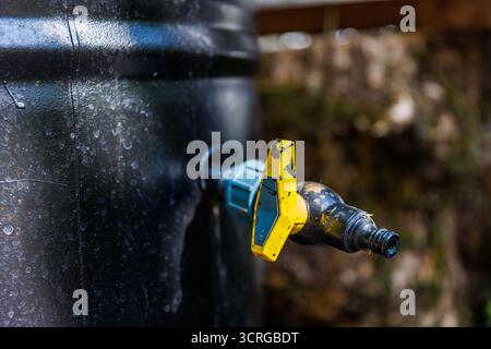 Nahaufnahme eines Wasserhahns mit leuchtenden gelben und blauen Farben, die Wassertropfen zeigen. Das Bild zeigt wesentliche Elemente des Wasserkonservats Stockfoto
