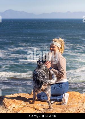 Eine Frau mit einem australischen Rinderhund (Blue Heeler) im Freien, der zusammen mit dem Hund aufspringt und sie küsst Stockfoto