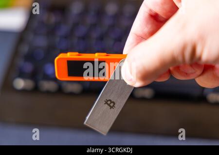 Erwachsene Menschen konzentrieren sich auf orangefarbene elektronische Geräte und Metall-Bitcoin-Schlüssel in modernen Büros. Die Tageseinstellung betont die technologische Stimmung und die ernste Demut Stockfoto