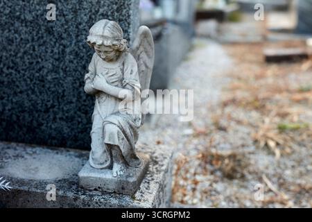 Eine kniende Engelsstatue ziert einen Grabstein auf einem Friedhof. Stockfoto
