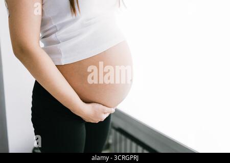 Nahaufnahme des schwangeren Bauches einer jungen Kaukasierin in weißem Tank Top Stockfoto
