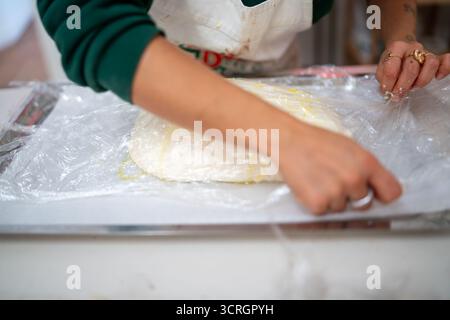 Die Hände einer Person wickeln vorsichtig einen Hügel mit ungekochtem Teig in Plastikfolie auf eine zum Backen vorbereitete Arbeitsplatte Stockfoto