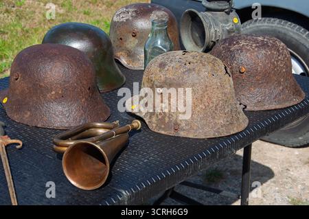 Alte Militärhelme und ein Bugle werden auf einem Tisch ausgestellt, wahrscheinlich zum Verkauf oder zur Ausstellung. Stockfoto