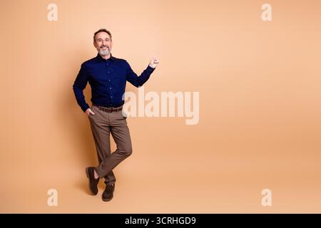Selbstbewusster, reifer Geschäftsmann, der vor beigefarbenem Hintergrund zur Seite zeigt, in professioneller Kleidung gekleidet und Erfolg zeigt Stockfoto