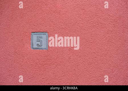 Zahl 5 auf strukturierter rosafarbener Stuckwand geprägt. Geprägtes Haus Nr. 5 auf einer leuchtend pinkfarbenen Stuckwand. Stockfoto