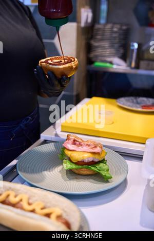 Koch, der eine Sauce auf ein Burgerbrötchen gibt Stockfoto