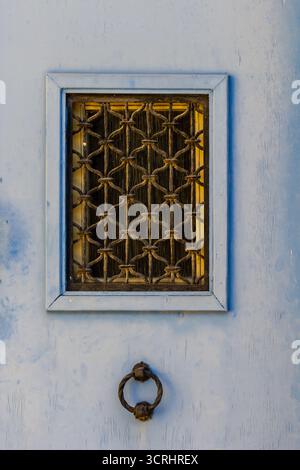 Blaue Tür mit schmiedeeisernem Gitterfenster und rustikalem Ringklopfer an der Fassade Stockfoto