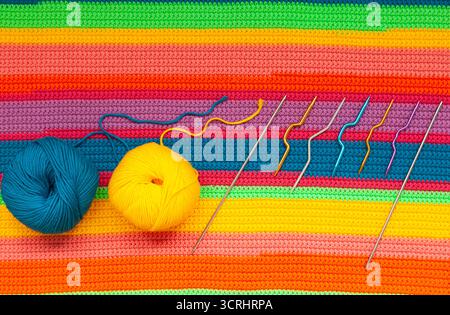 Knitted multi-colored handmade fabric with balls of yellow, blue threads and knitting needles. Stockfoto