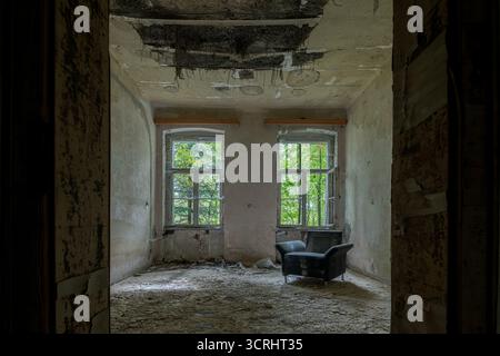 Verlassenes Zimmer mit Vintage-Sessel und Sofa in der Nähe eines kaputten Fensters, Stadtfotografie mit natürlichem Licht Stockfoto