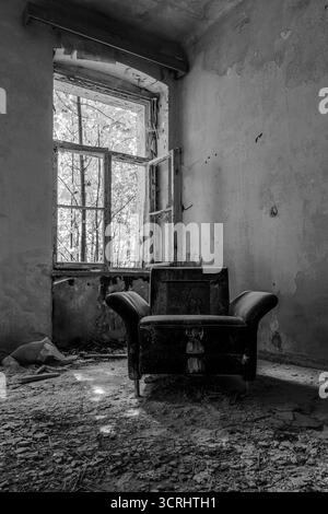 Verlassenes Zimmer mit Vintage-Sessel und Sofa in der Nähe eines kaputten Fensters, Stadtfotografie mit natürlichem Licht Stockfoto