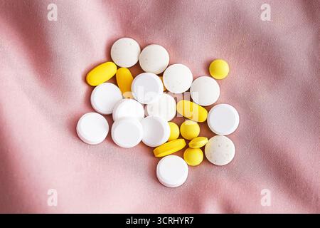 Weiße und gelbe Pillen auf rosafarbenem Stoff. Arzneimitteltabletten und Vitamine auf textilem Hintergrund. Pharmazeutische Ergänzungen für Gesundheit und Behandlung. Stockfoto