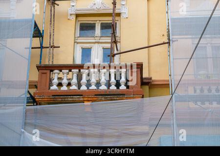 Nahaufnahme eines alten Balkons mit Balustrade und altem Fenster, umgeben von Gerüsten und Schutznetz, zeigt Renovierungsarbeiten an einem historischen Gebäude Stockfoto