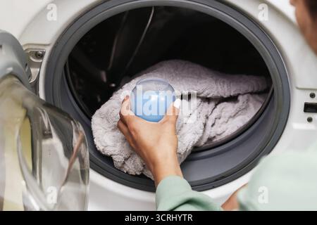 Frau, die Waschmittel in die Waschmaschine bringt. Hausarbeit und Reinigungsroutine. Haushaltsgeräte für Hygiene und frische Kleidung. Stockfoto