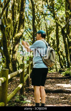 Kaukasischer älterer Mann, der Lorbeerwald erforscht und mit dem Telefon fotografiert Stockfoto