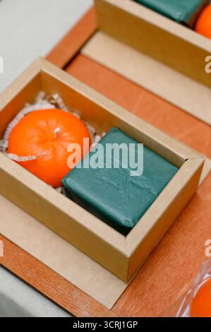 Handgefertigtes Neujahrs-Souvenir mit einer Kerze in Form einer Mandarine und Seife. Blick von oben auf die Bastelbox mit handgefertigten Geschenken auf hölzernem Hintergrund. Stockfoto
