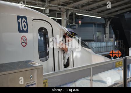 Japanischer Zugbegleiter in Uniform am Bahnsteig. Professionelles Eisenbahnpersonal, das einen effizienten Service auf Japans pünktlichen Transport bietet Stockfoto