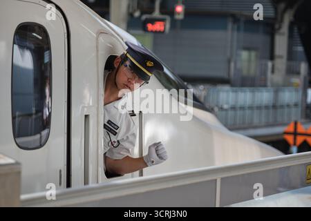 Japanischer Zugbegleiter in Uniform am Bahnsteig. Professionelles Eisenbahnpersonal, das einen effizienten Service auf Japans pünktlichen Transport bietet Stockfoto