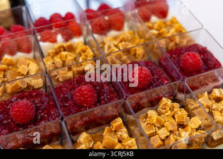 Mini-Himbeer- und Karamell-Dessertbecher Nahaufnahme. Nahaufnahme eleganter Desserttassen gefüllt mit Himbeerkompott, Karamellstückchen und Sahne, angeordnet Stockfoto