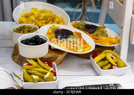 Vorspeisenplatte mit geräuchertem Käse, Oliven und gefüllten Paprika. Rustikale Vorspeise mit geräucherten Käsestreifen, schwarzen und grünen Oliven, gefüllt Stockfoto