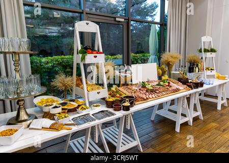 Rustikaler Buffettisch mit Aufschnitt, Käse und Vorspeisen. Elegantes Buffet mit Aufschnitt, geräucherten Käse, Brot, Oliven und eingelegtem Gemüse Stockfoto