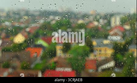 Regentropfen auf Fensterglas mit verschwommenem Hintergrund in der Stadt, flacher Freiheitsgrad. Regentropfen sind über eine Fensterscheibe verstreut, mit einer verschwommenen Stadtlandschaft Stockfoto