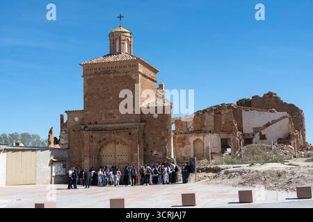 Eine Gruppe von Menschen versammelte sich vor einer historischen Backsteinkirche mit einem Kreuz auf der Spitze, umgeben von Ruinen unter einem klaren blauen Himmel Stockfoto