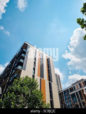 In einem modernen Wohnviertel in den Himmel blickend. Farbenfrohe Hochhäuser mit Fassaden, die mit grauen, orangen und beigen Streifen verziert sind. Stockfoto