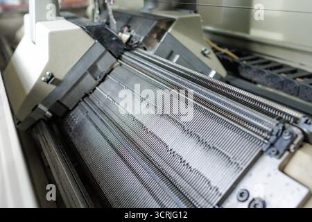 Nahaufnahme einer industriellen Strickmaschine Nadelbett-Formschlaufen in einer Textilfabrik, die Präzisionsautomatisierung und Qualitätsfertigung hervorhebt Stockfoto