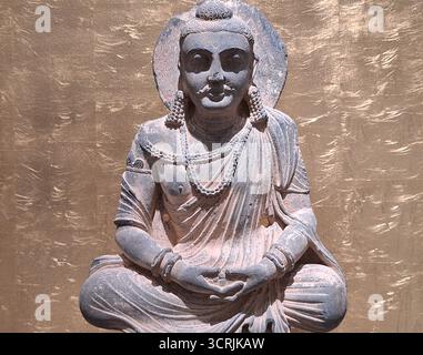 Buddhistische Meditationskunst: Nahaufnahme der meditierenden Bodhisattva-Statue vor einem kunstvollen goldenen Hintergrund in einem asiatischen Tempel Stockfoto