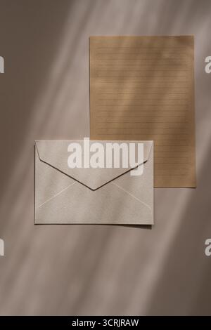 Beigefarbener Umschlag und Kraftpapier. Minimalistisches Schreibwarenset mit einem beigefarbenen, strukturierten Umschlag und einem linierten Kraftpapier-Blatt auf beigefarbenem Hintergrund mit Stockfoto