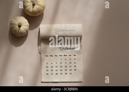 Kalender aus Leinenstoff mit Oktobermonat, dekorativen Kürbissen, weichen Schatten, beigefarbenem Hintergrund, Herbstästhetik von oben Stockfoto