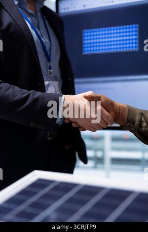 Geschäftsleute in Industriebetrieben schütteln die Hand, reden über industrielle Energielösungen, Nahaufnahme. Investor und Manager einer Photovoltaik-Fabrik machen Handshake, nachdem sie sich auf die Designs von Solarmodulen geeinigt haben Stockfoto